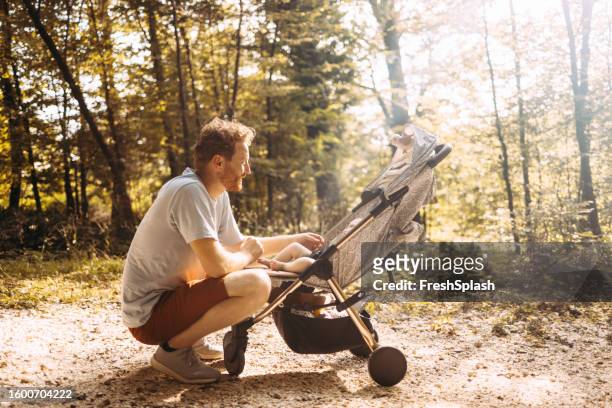 young caucasian dad squatting by his newborn baby's stroller during a walk in the park - baby pram in the park bildbanksfoton och bilder