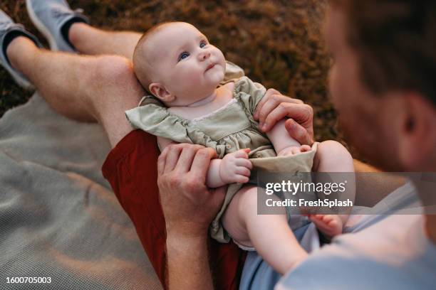 unrecognizable caucasian dad holding his smiling baby on his lap and playing with her - op schoot stockfoto's en -beelden