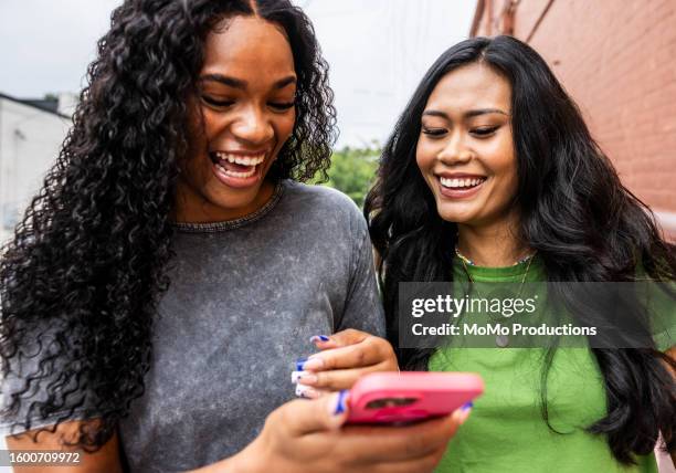 two young women walking down urban street and using smartphone - heaven icon stock pictures, royalty-free photos & images