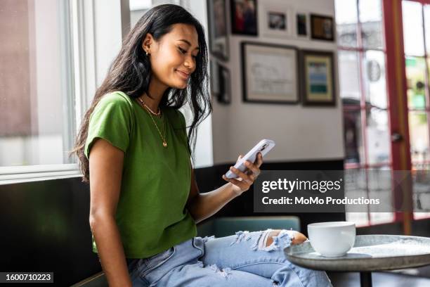 young woman using smartphone in coffeeshop - paiement en ligne photos et images de collection