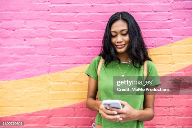 young generation z woman standing against brightly colored wall and using smartphone - millennial generation stock pictures, royalty-free photos & images