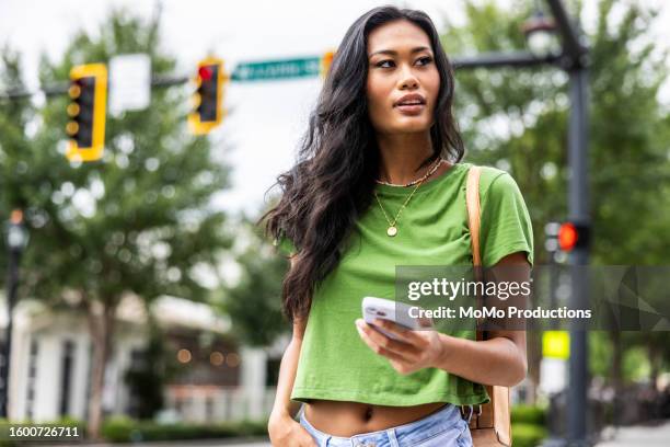 young woman walking down urban street and using smartphone - tshirt icon stock-fotos und bilder