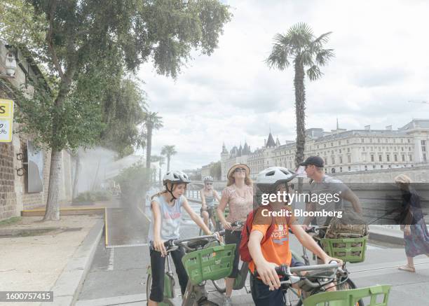 Tourists ride hire bicycles ride through water mists on the banks of the River Seine in central Paris, France, on Monday, Aug. 14, 2023. July was...