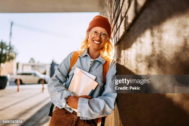 portrait of smiling young beautiful woman leaning on brick wall - studente stockfoto's en -beelden