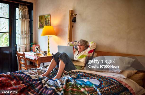 senior woman relaxing on bed with laptop - comfortable retirement stock pictures, royalty-free photos & images