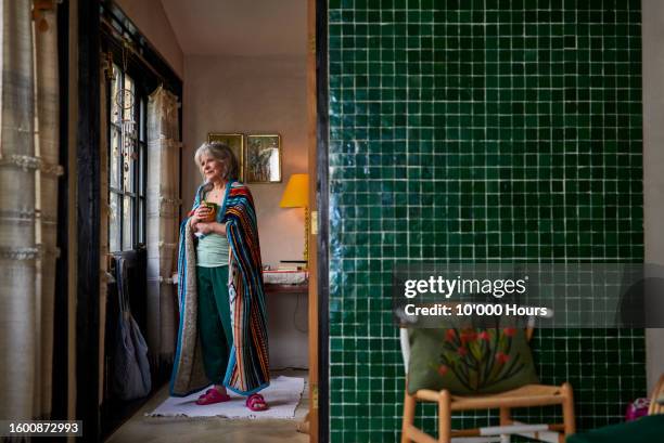 senior woman standing looking out of window at home - escaping room stock pictures, royalty-free photos & images