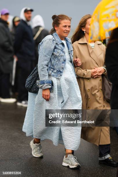 Guest wears a pale blue ruffled embossed long dress, a blue faded denim jacket, a black with gray flower print pattern fabric shoulder bag, brown...