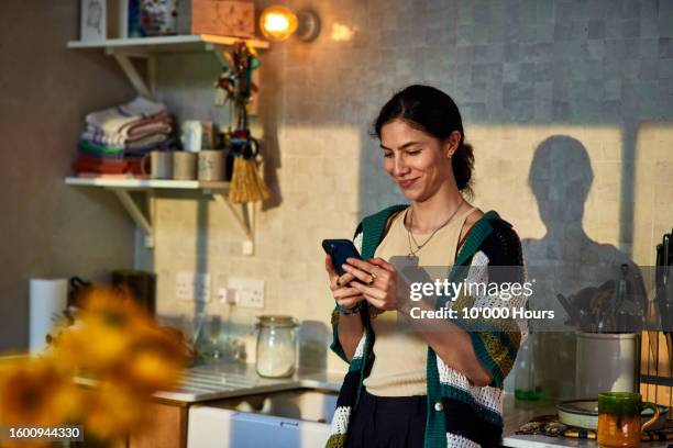 smiling mid adult woman using social media on smart phone - home interior stock pictures, royalty-free photos & images