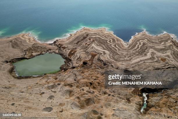 An aerial picture taken on August 15, 2023 shows patterns formed by crystalized minerals and sinkholes on the surface of a dried-up Dead Sea area...
