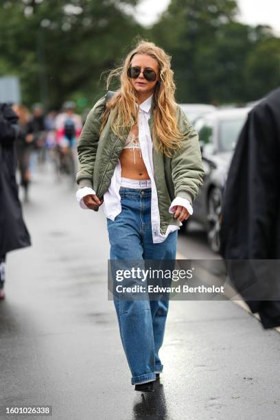 Guest wears black aviator sunglasses, a white shirt, a white lace print pattern V-neck bra underwear, a pale khaki bomber coat, white silk panties...