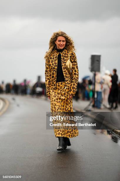 Emili Sindlev wears a black turtleneck pullover, a beige with brown and black leopard print pattern fur zipper jacket, matching beige with brown and...