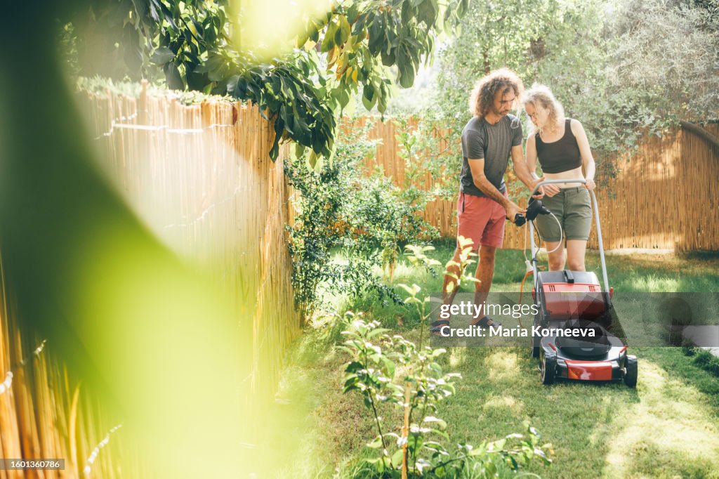 Couple taking care of their lawn. Couple cutting the grass in the Backyard.