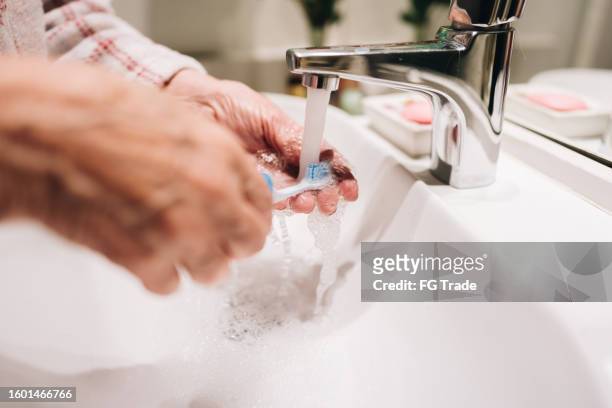close-up of a senior washing toothbrush in the bathroom - escova de dentes imagens e fotografias de stock