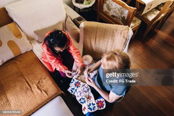 blick aus der vogelperspektive auf ältere freunde, die zu hause im wohnzimmer häkeln - assisted living stock-fotos und bilder