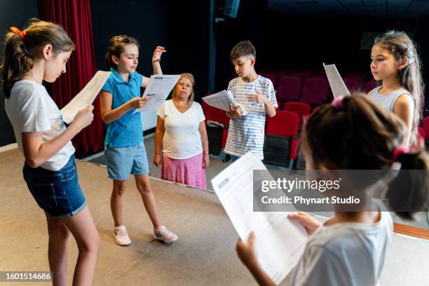 gruppe von kindern, die die probe des theaterclubs genießen. sie lesen mit ihrem schauspiellehrer das drehbuch. - children theater stock-fotos und bilder