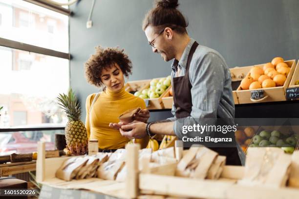 mitarbeiter eines bio-lebensmittelgeschäfts hilft einem kunden - gemüseladen stock-fotos und bilder