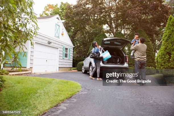 family standing near car on driveway outside house - oprit stockfoto's en -beelden