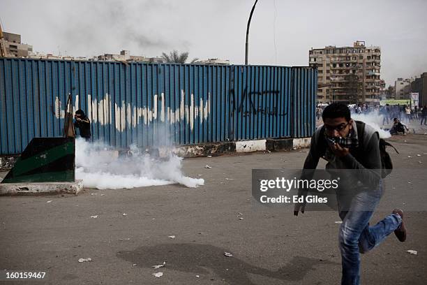 Egyptian protesters run away from tear gas canisters fired by riot police during a demonstration in Tahrir Square on January 27, 2013 in Cairo,...