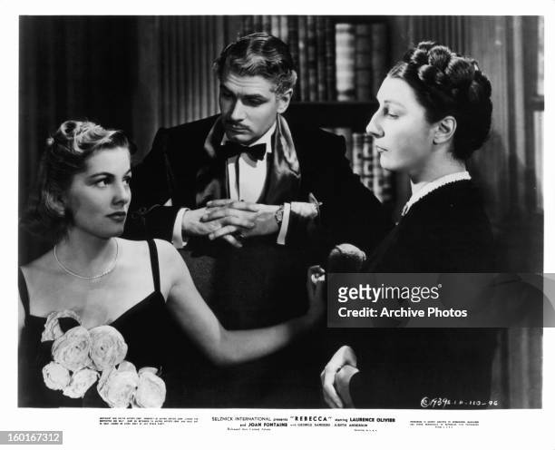 Joan Fontaine and Judith Anderson stare at each other while Laurence Olivier stands in the middle of them with his hands folded in a scene from the...