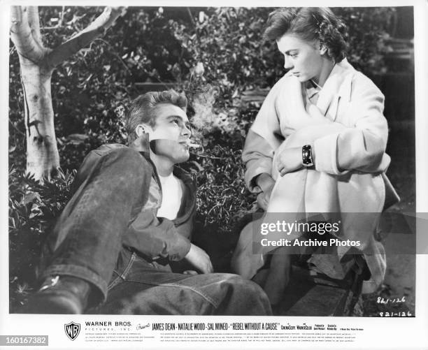 James Dean reclined on the ground with a cigarette in his mouth, looks up at Natalie Wood in a scene from the film 'Rebel Without A Cause', 1955.