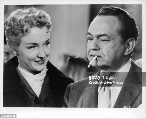 Edward G Robinson stand with a cigarette in his mouth as Nina Foch stands next to him in a scene from the film 'Illegal', 1955.