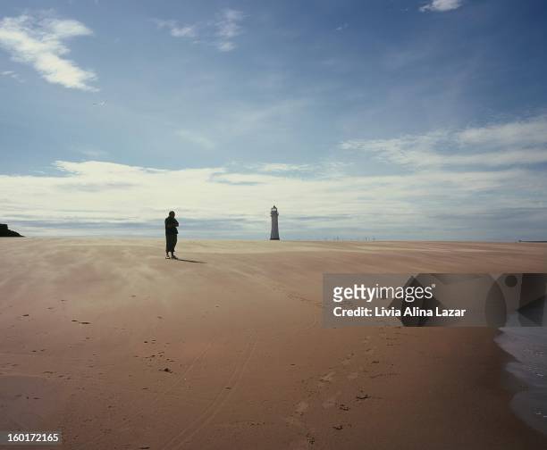 Silhouette of a meditative man on the shore; sand beach with a lighthouse. New Brighton.