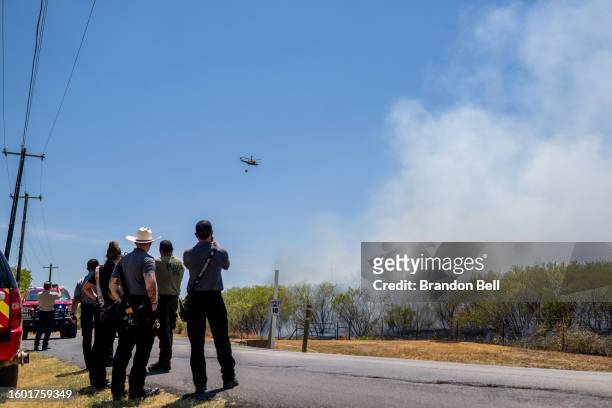 Members of the Hays County Emergency Service Districts and the Kyle and Buda Fire Departments look on as a helicopter prepares to drop water on a...