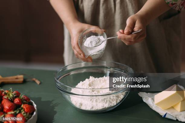 an unrecognizable woman adding spoons of flour into a bowl while preparing some dessert - flour stock pictures, royalty-free photos & images