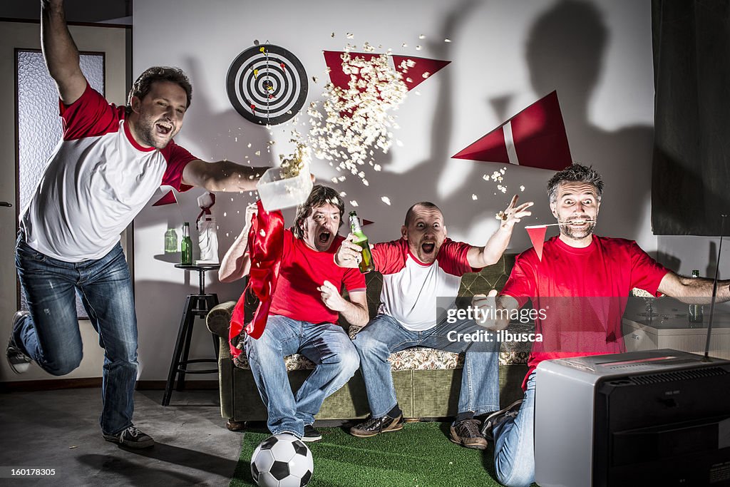 Four young adult men friends watching football on television: Goal!