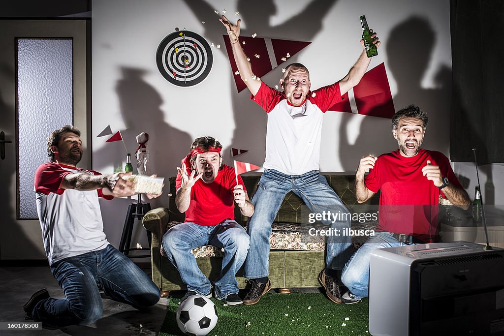 Four young adult men friends watching football on television: Goal!