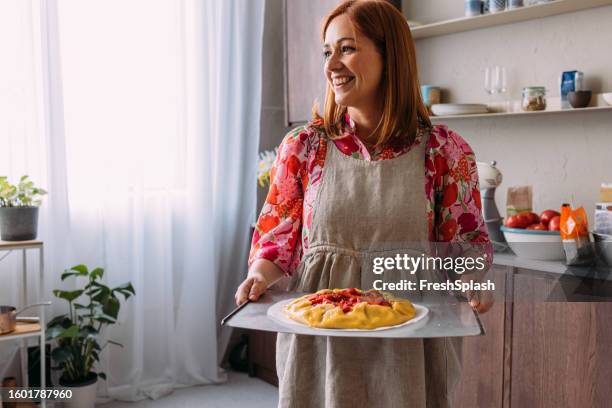 a happy beautiful ginger woman with an apron looking away after making a strawberry tart - tart dessert stock pictures, royalty-free photos & images