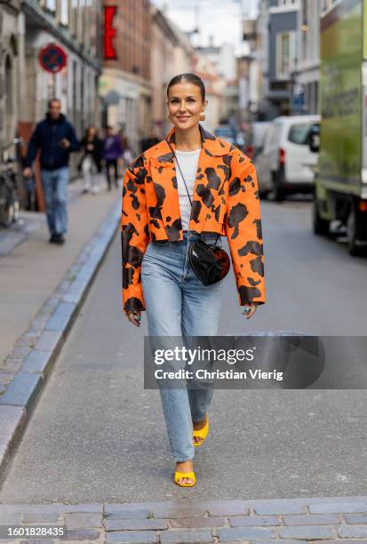 Nina Sandbech wears denim jeans, black heat shaped bag, orange black bag with cow print, yellow heels, golden earrings during the Copenhagen Fashion...