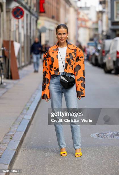 Nina Sandbech wears denim jeans, black heat shaped bag, orange black bag with cow print, yellow heels, golden earrings during the Copenhagen Fashion...