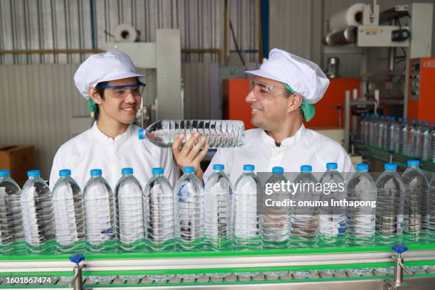 quality control inspector specialist man checking a bottle of drinking water on the conveyer production line in processing drinking water manufacturing - bottling plant stock pictures, royalty-free photos & images