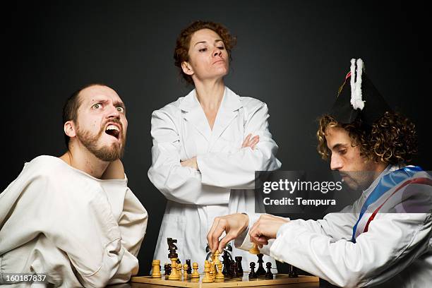 medical professional overseeing a chess game. one player is in a strait jacket and the other is in fancy dress - dwangbuis stockfoto's en -beelden