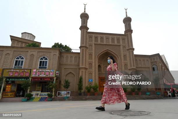 This picture taken on July 19, 2023 shows a woman passing an old disused mosque in Artux, northwestern China's Xinjiang region.