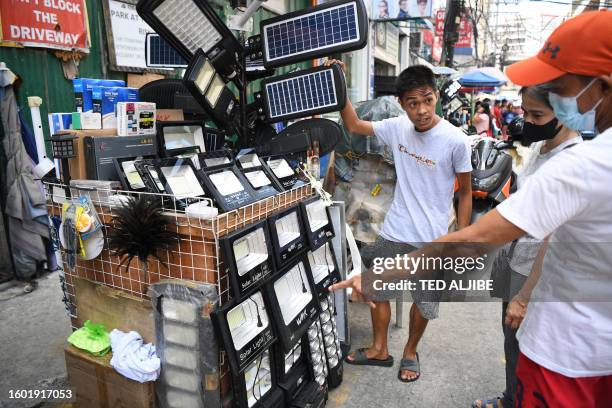 Vendor selling solar-powered house and street lights assists customers along a street in Manila on August 16, 2023.