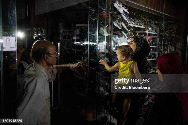 Shoe store owner speaks with customers by smartphone torch light outside his store during a loadshedding power outage period, in the El-Sayeda Zainab...