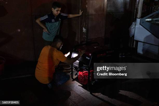 Vendor uses a smartphone torch light as he attempts to power-on an emergency generator outside a store during a loadshedding power outage period, in...