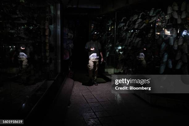 Shopkeeper uses a smartphone torch outside his shoe store during a loadshedding power outage period, in the El-Sayeda Zainab district of Cairo,...