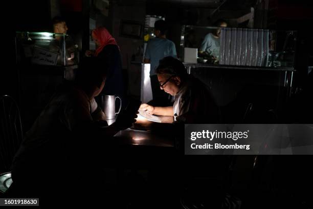 Customer browses a menu by smartphone torch light inside an unlit restaurant during a loadshedding power outage period, in the Al-Muneera district of...