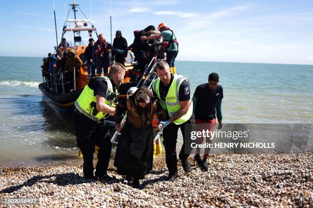 An interforce officer and a border force officer help a woman on the beach at Dungeness on the southeast coast of England, on August 16 after she...