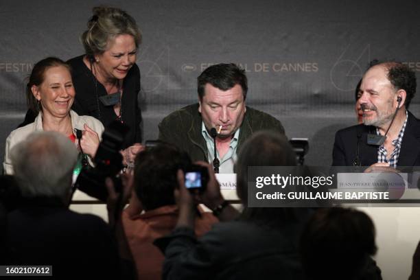 Finnish director Aki Kaurismaki puts a lit cigarette inside his mouth next to French actor Jean-Pierre Darroussin and Finnish actress Kati Outinen as...