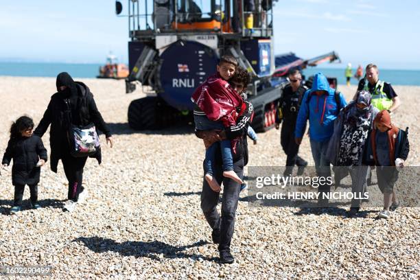 Man carrying a child in his arms, is followed by a migrant pregnant woman , as they walk on the beach at Dungeness on the southeast coast of England,...