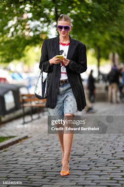 Marianne Theodorsen wears purple aviator plastic sunglasses, gold earrings, a silver and rhinestones large necklace, a white with red and black...