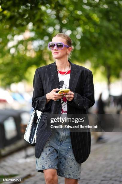 Marianne Theodorsen wears purple aviator plastic sunglasses, gold earrings, a silver and rhinestones large necklace, a white with red and black...