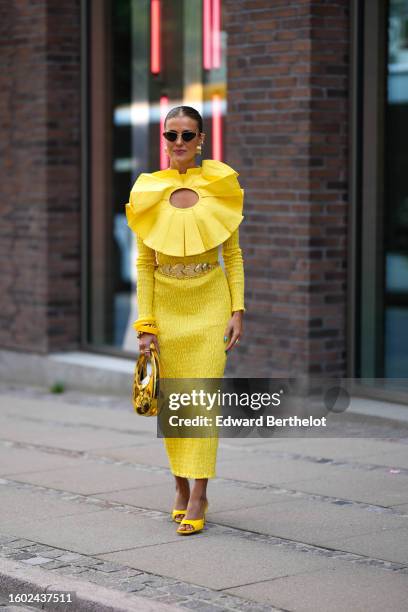 Nina Sandbech wears black and gold borders sunglasses, gold earrings, a yellow embroidered on the chest large ruffled large circle cut-out at the...