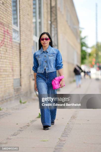 Miki Cheung wears neon pink squared sunglasses, gold and white pearls earrings, a blue faded denim buttoned jacket, blue faded denim with embroidered...