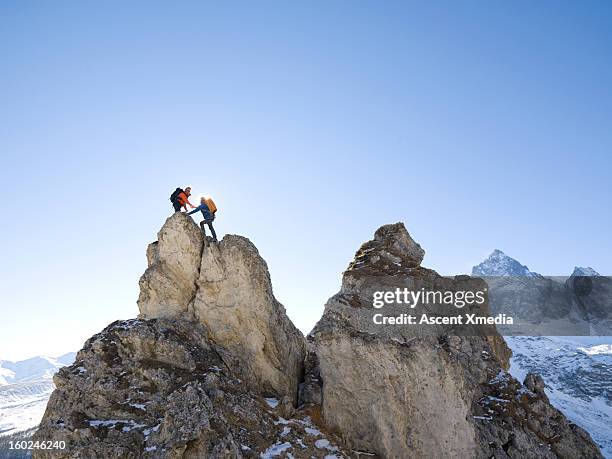 mountaineer offers helping hand to teammate,summit - alpinismo foto e immagini stock