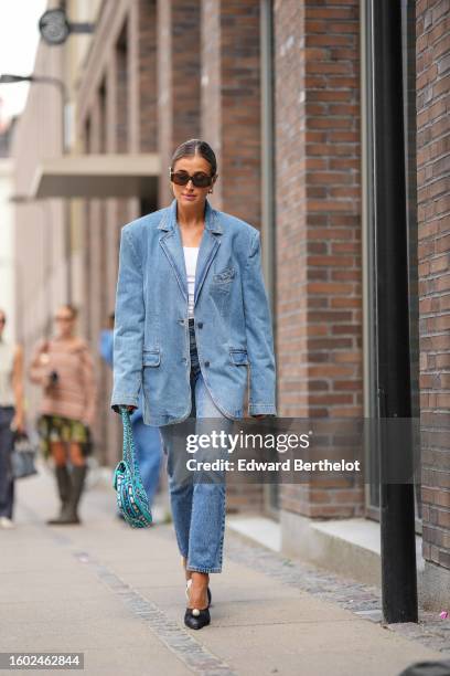 Darja Barannik wears brown marble sunglasses from Celine, gold earrings, a blue denim oversized blazer jacket, matching blue denim large pants, a...